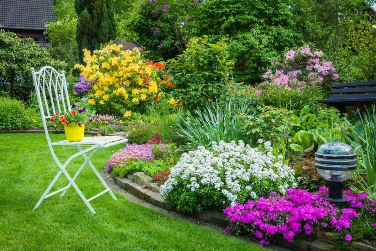 jardin paysager avec chaise de jardin et massifs de fleurs violettes blanches et jaunes