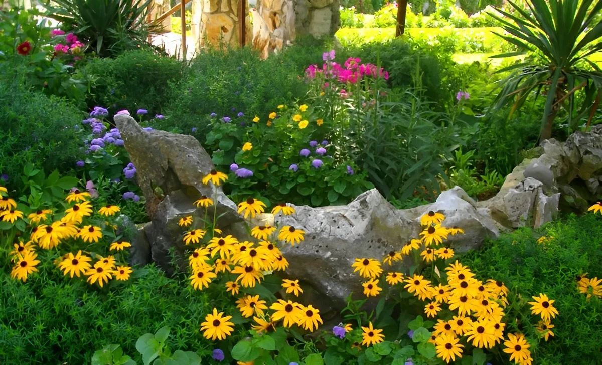 le rocher gris neutre au milieu du jardin verdoyant avec des fleurs jaunes au premier plan