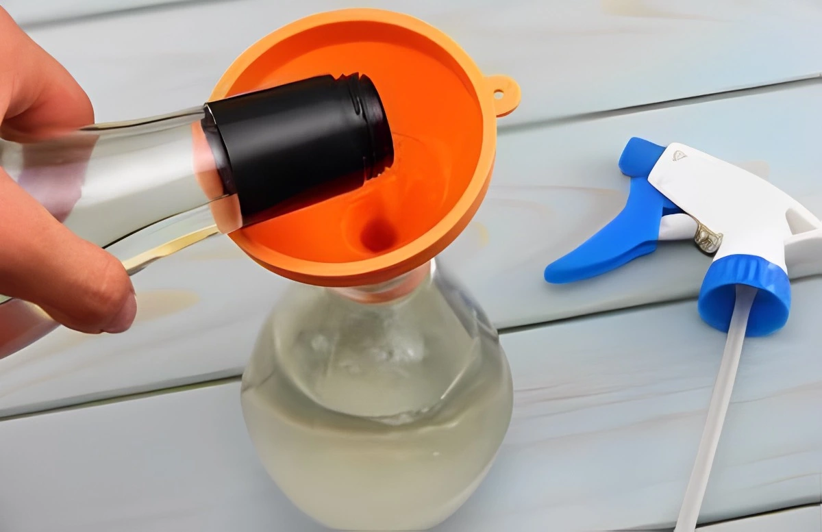 verser du vinaigre d une bouteille avec un entonnoir orange dans un recipient a pulverisateur pose a droite