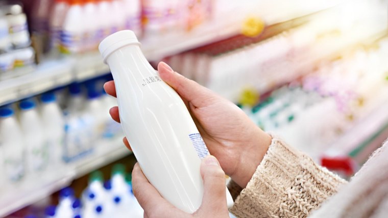 bouteille de lait avec une date de peremption tenue dans les deux mains devant un rayon au supermarche