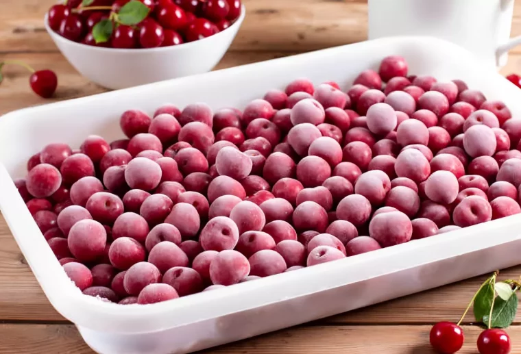 cerises surgelees dans un bac en plastique rectangulaire avec une paire de cerise devant et un bol pleine de cerises derriere