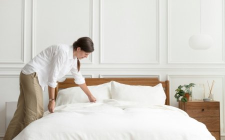 chambre lit draps blancs table chevet bois plante verte lampadaire blanc femme nettoyage