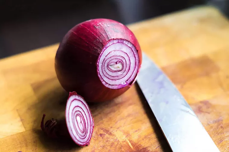 gros plan d un oignon rouge entier avec un petit bout coupe sur une planche en bois