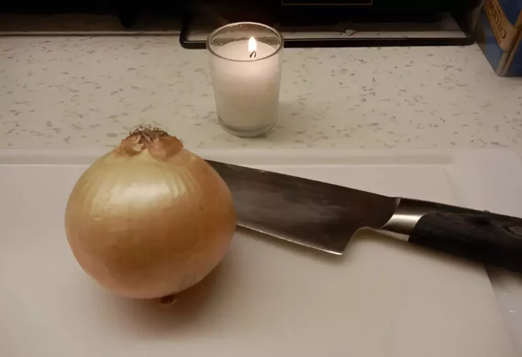 oignon entier et un couteau sur une planche blanche et une bougie allumee a cote