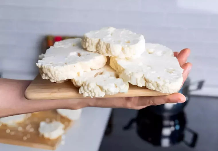 plusieurs tranches de fromage frais sur une planchette en bois tenant dans une main