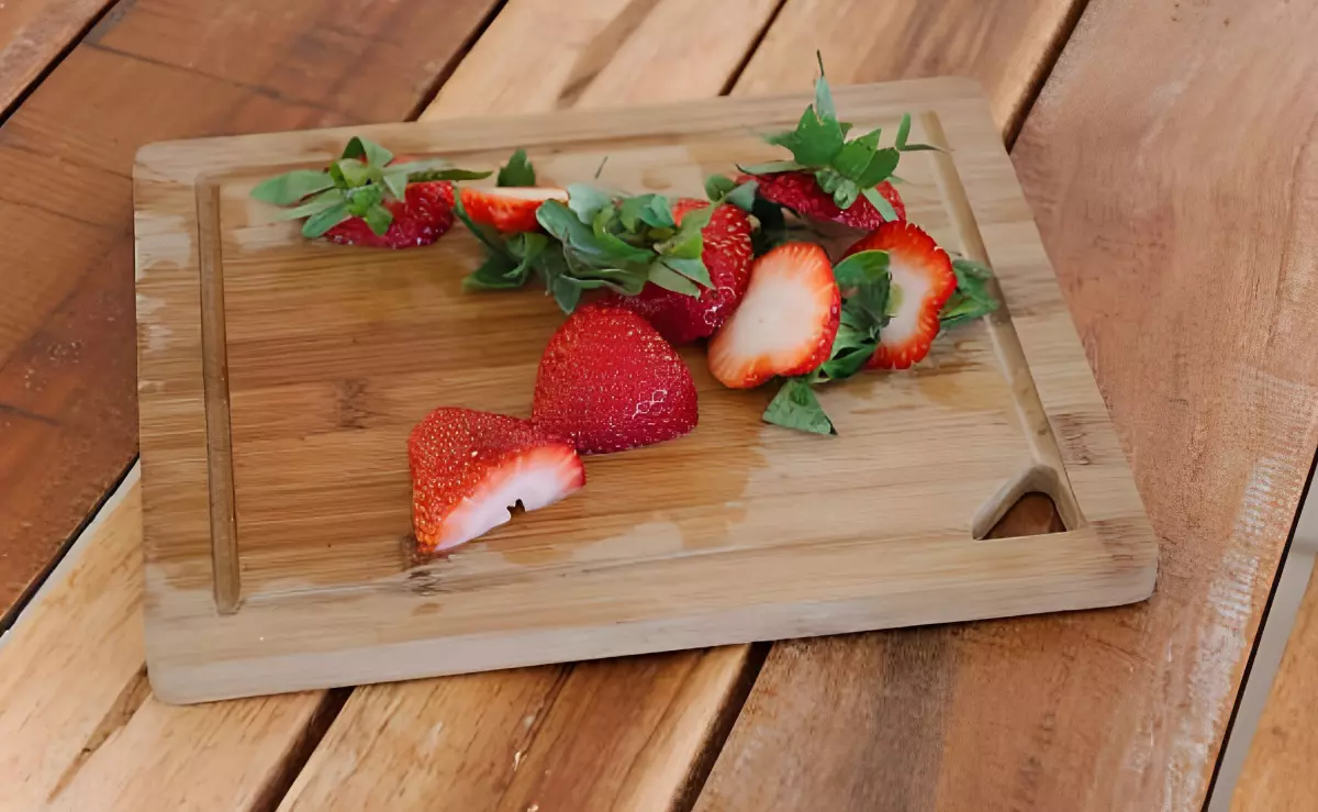 queues de fraises et deux morceaux de fraises decoupees devant elles sur une planche en bois