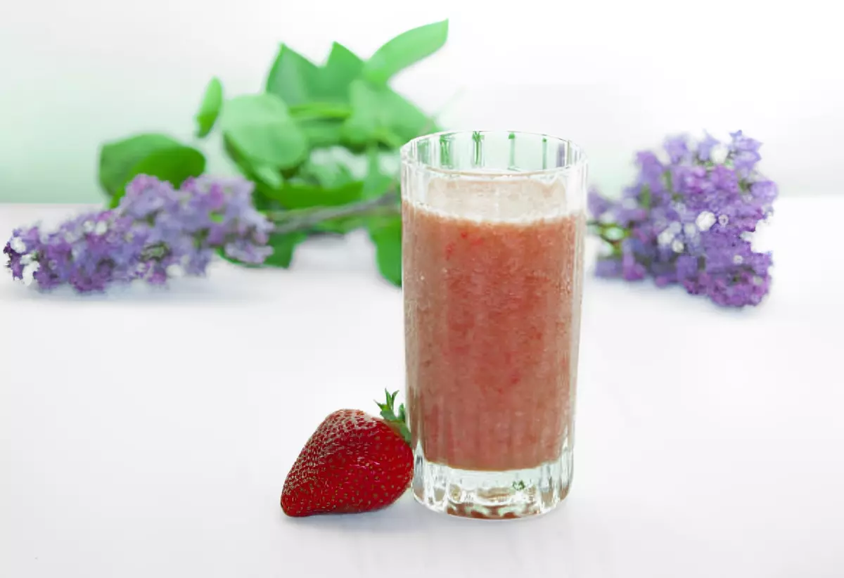 smoothie dans un verre avec une fraise a cote sur fond blanc avec deux fleurs de lilas