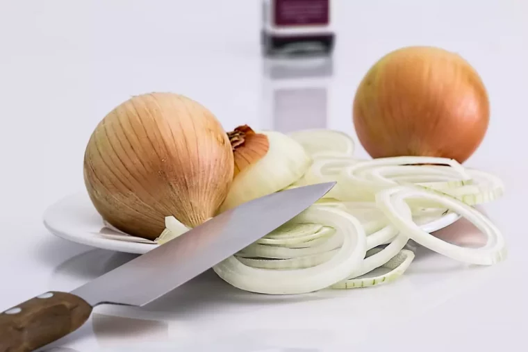 un couteau en premier plan avec deux oignons entiers et un coupe en rondelles dans une assiette blanche sur fond blanc