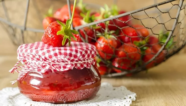 un pot de confiture avec une fraise fraiche par dessus sur fond d une corbeille de fraises fraiches floues
