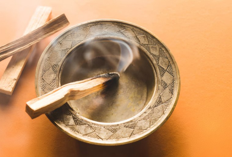 extremite de palo santo allume dans une assiette couleur bois sur fond orange