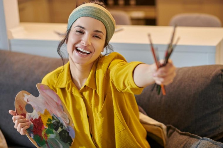 femme sourire canape peinture outils palette chemise jaune moutarde