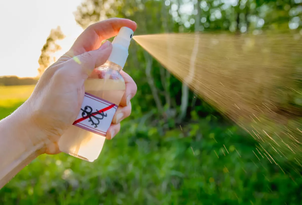 main qui vaporise avec un spray transparent avec une etiquette avec un symbole anti moustiques