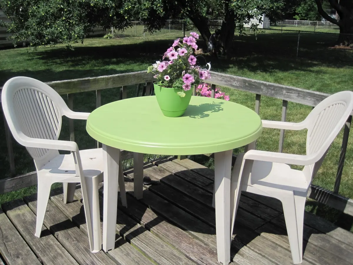 table ronde vert plastique chaises blanches pot vert fleurs cloture bois terrasse