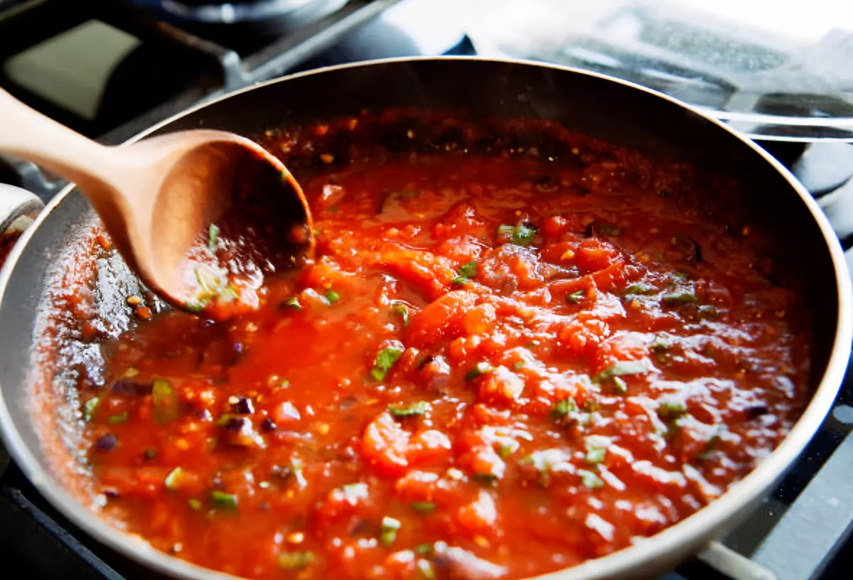 une sauce tomate en train de cueillir dans une poele et une grosse cuillere en bois