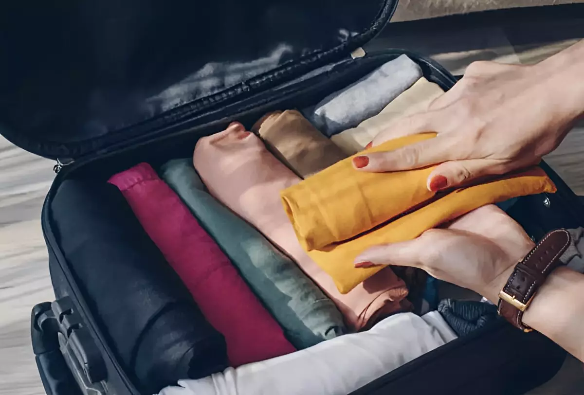 valise ouverte remplie de vêtement enroules et des mains qui pose un autre
