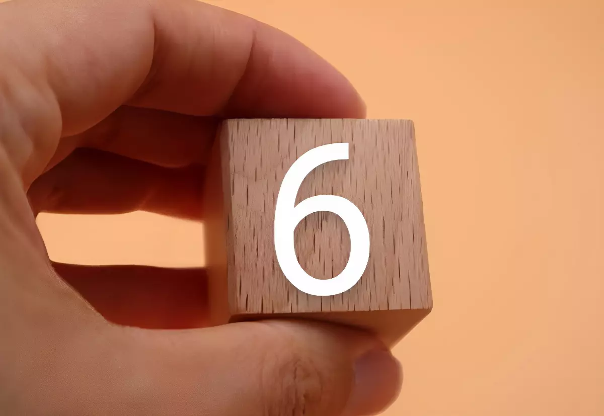 chiffre six sur cube en bois tenu par une main sur fond couleur peche