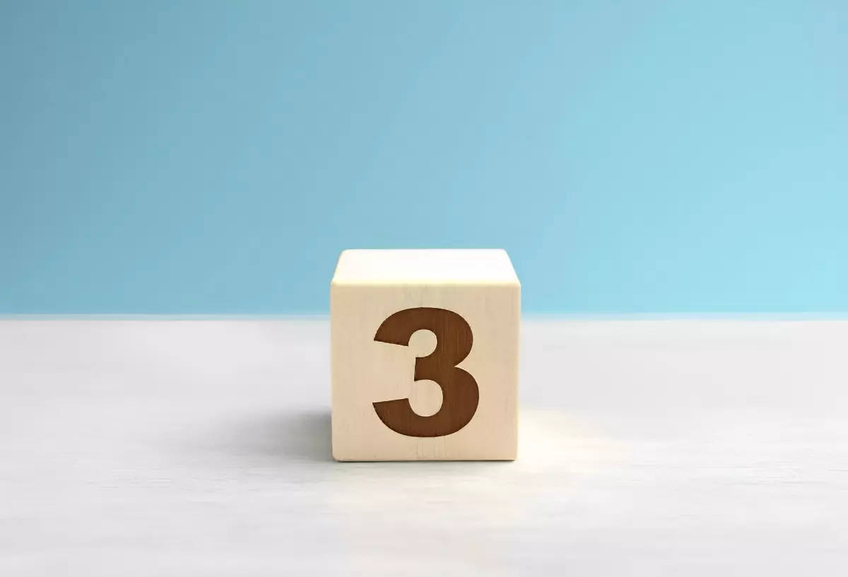 chiffre trois sur un cube en bois au centre de l image sur une surface blanche et fond bleu