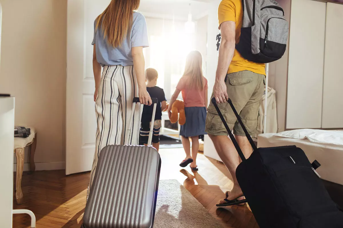 famille avec deux enfants qui part en vacances avec une valise grise et une noire