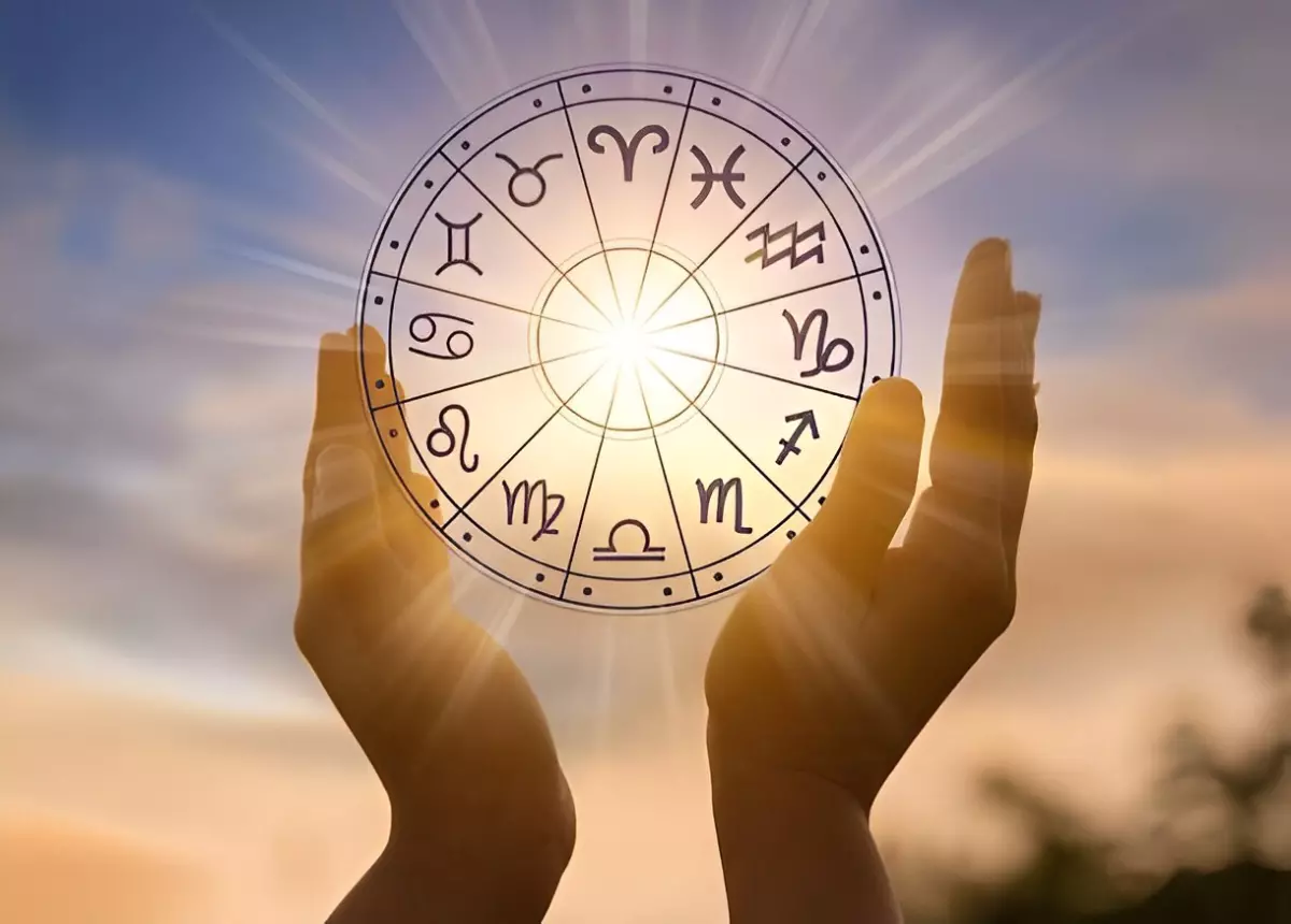 le cercle des douze signes astrologiques tenu entre les mains sur fond du disque solaire dans le ciel