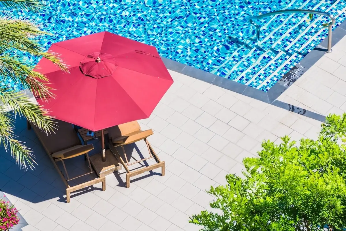 parasol rouge transat chaise longue bois arbres autour piscine revetement sol