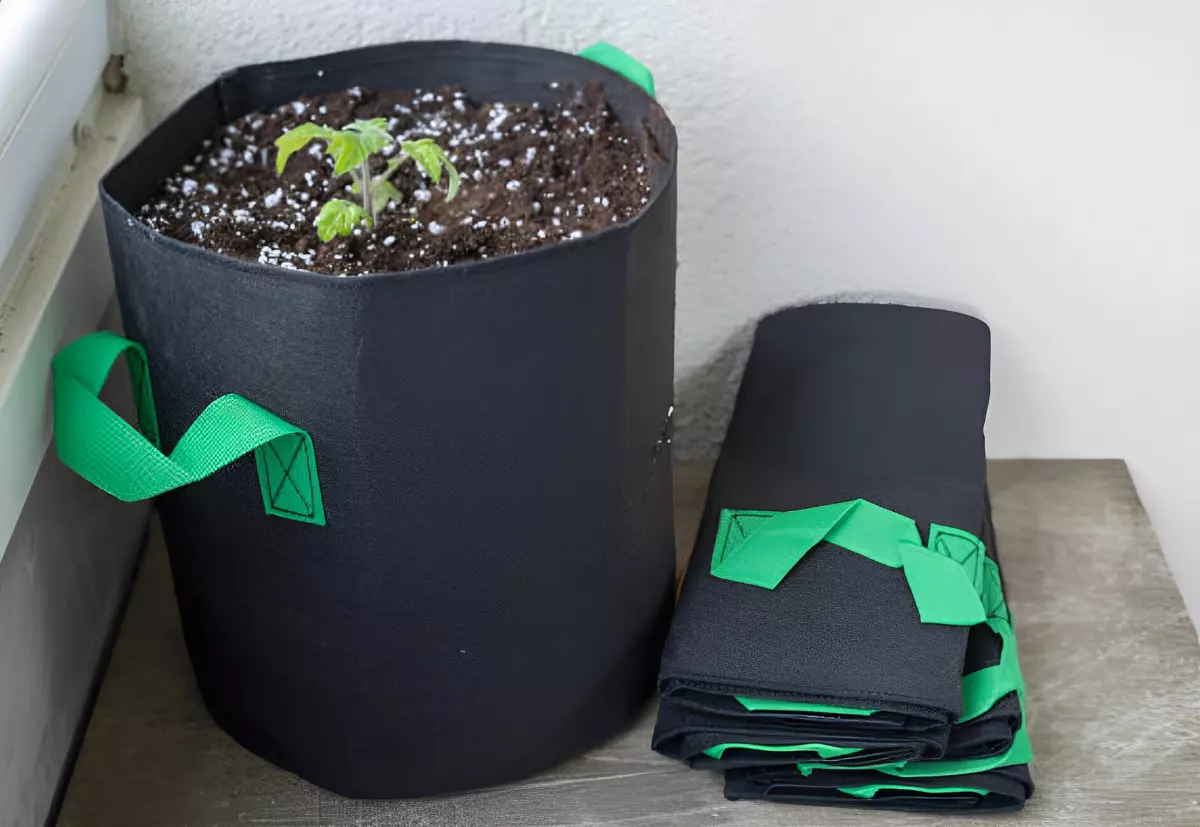 sacs de plantation noirs avec des poignees vertes poses au sol sur un balcon a cote d un sac rempli de terre avec une plante