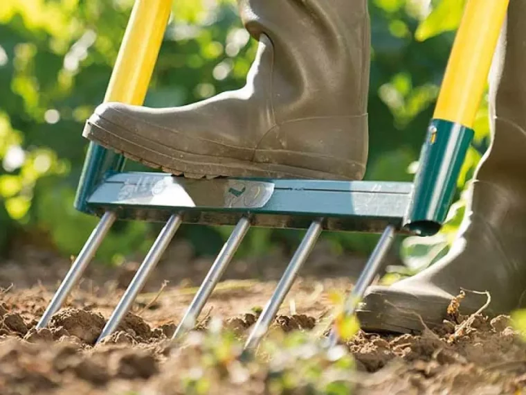 gros plan sur un outil de aeration de la terre la grelinette avec une botte dessus et des manches jaunes