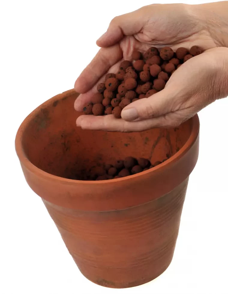 un pot en terre cuite sur fond blanc avec deux mains qui versent des billes d argile dedans