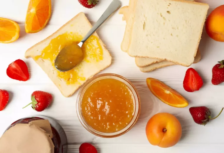 vue de dessus d un pot de confiture ouvert entoure de tranches de pain et de morceaux d orange fraises et abricots