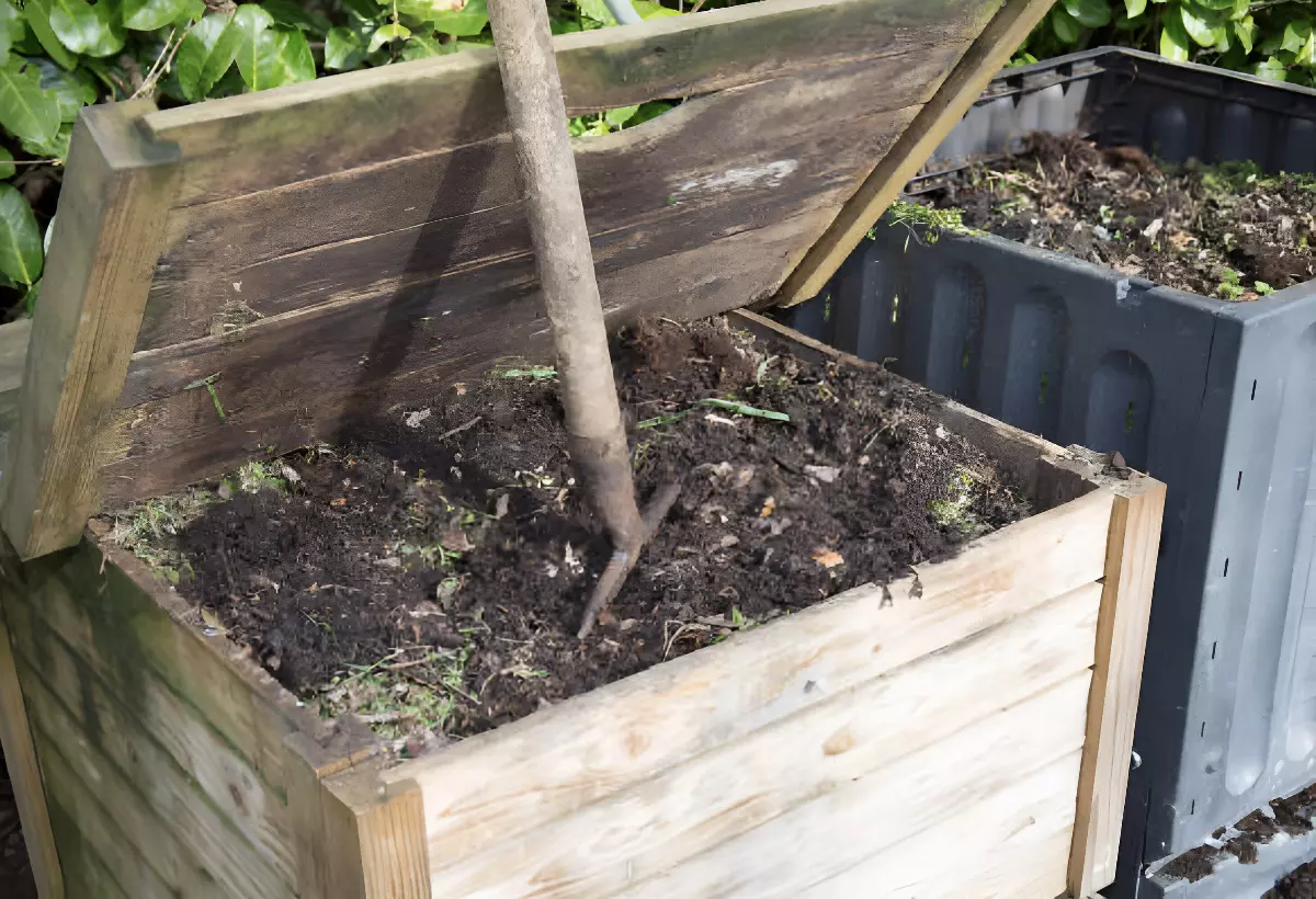 bac a compost en bois plein avec un couvercle ouvert et un outil de jardinage enfourche dedans