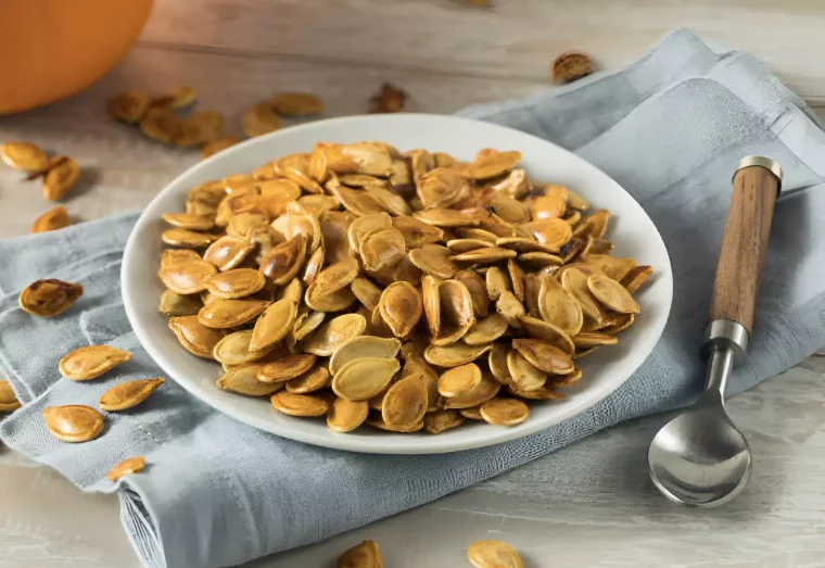 des graines de potiron roties avec la coque dans une assiette sur un torchon de cuisine avec une cuillere