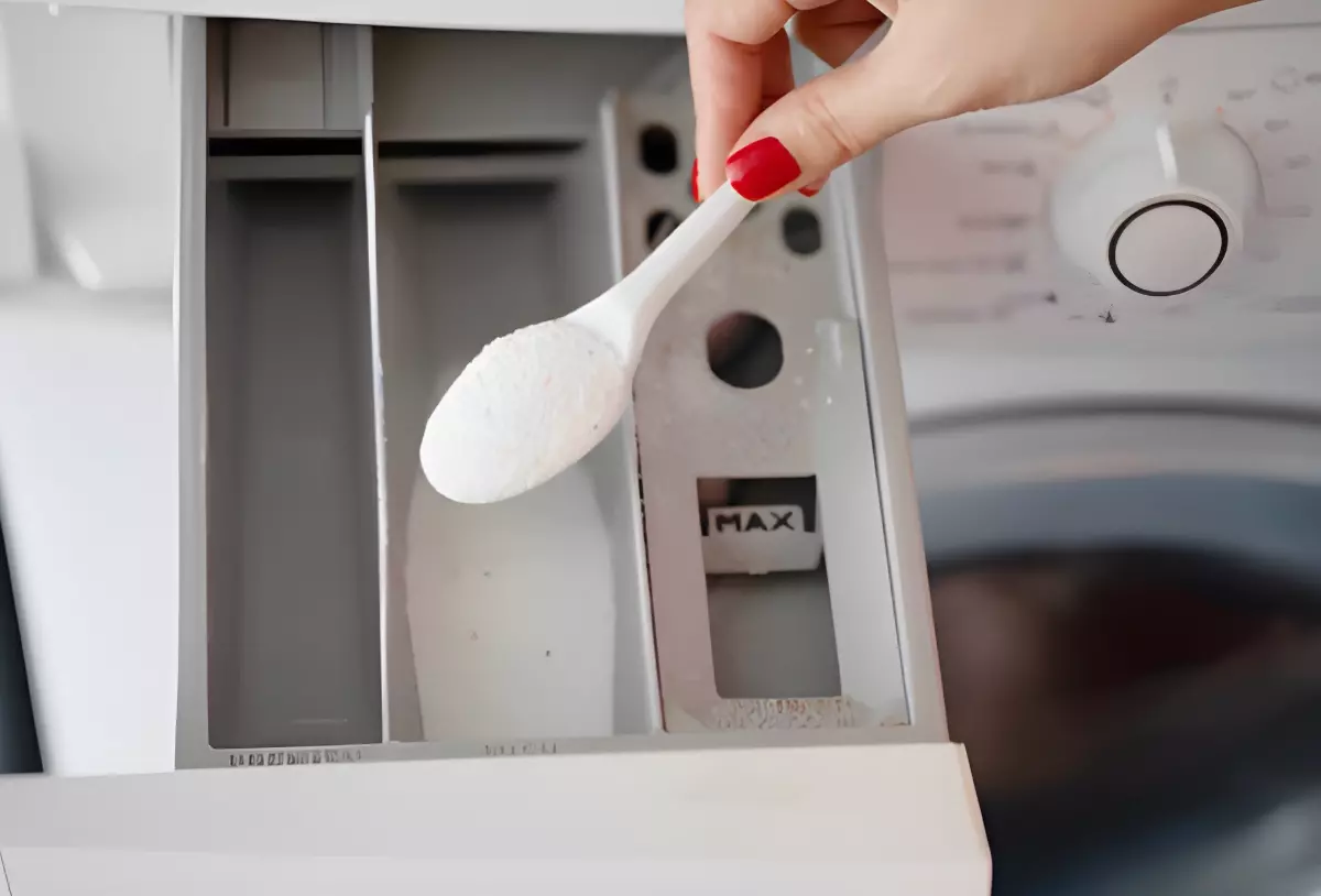 poudre blanche dans une cuillere au dessus du tiroir a lessive du lave linge