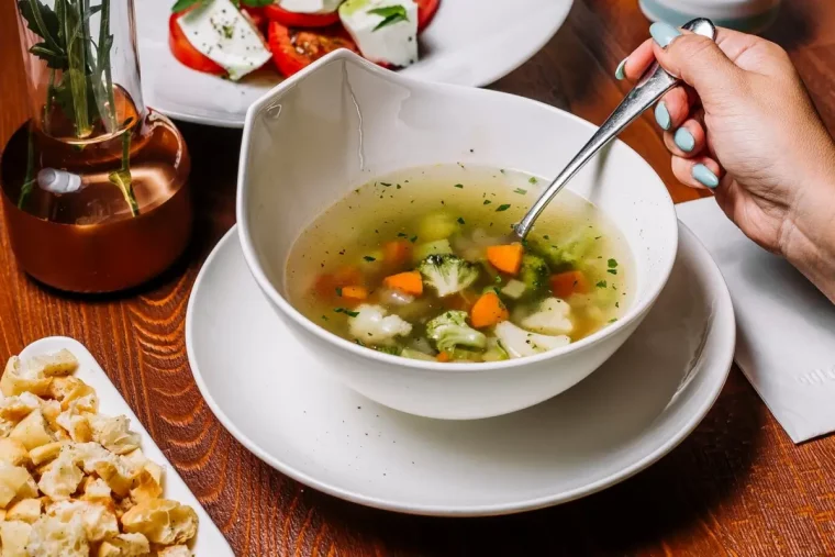 bol blanc sur table bois fonce assiette ronde blanche soupe feuilles de chou fleur carotte