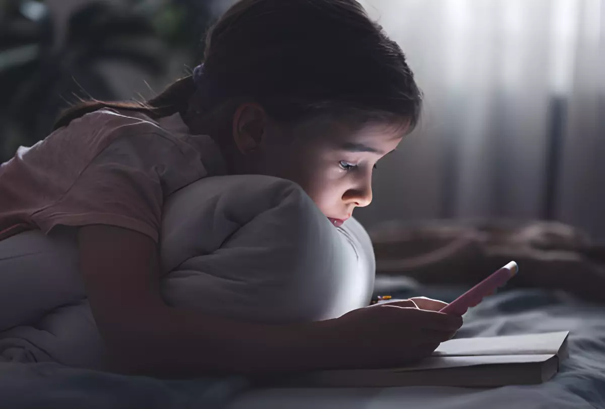 enfant allonge sur le ventre dans un lit avec un telephone portable
