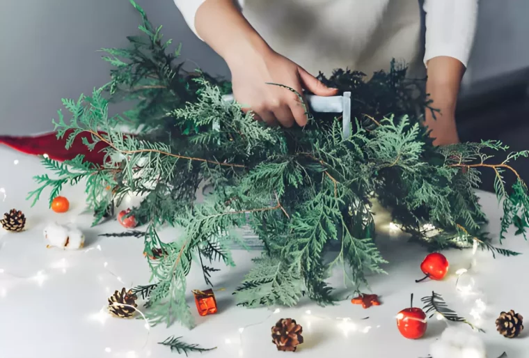 faire tenir des branches de sapin ensemble dans un recipient tenu par la manche par une main feminine