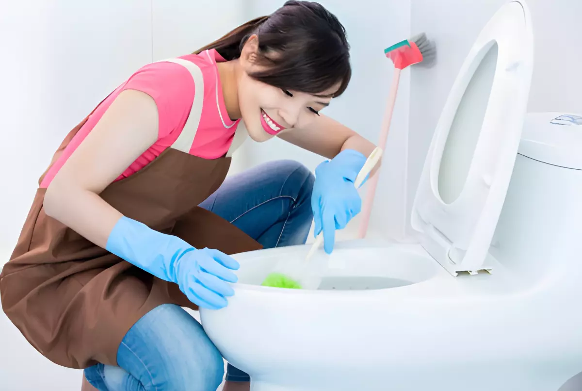 femme asiatique avec des gants bleues nettoie des toilettes avec le sourire