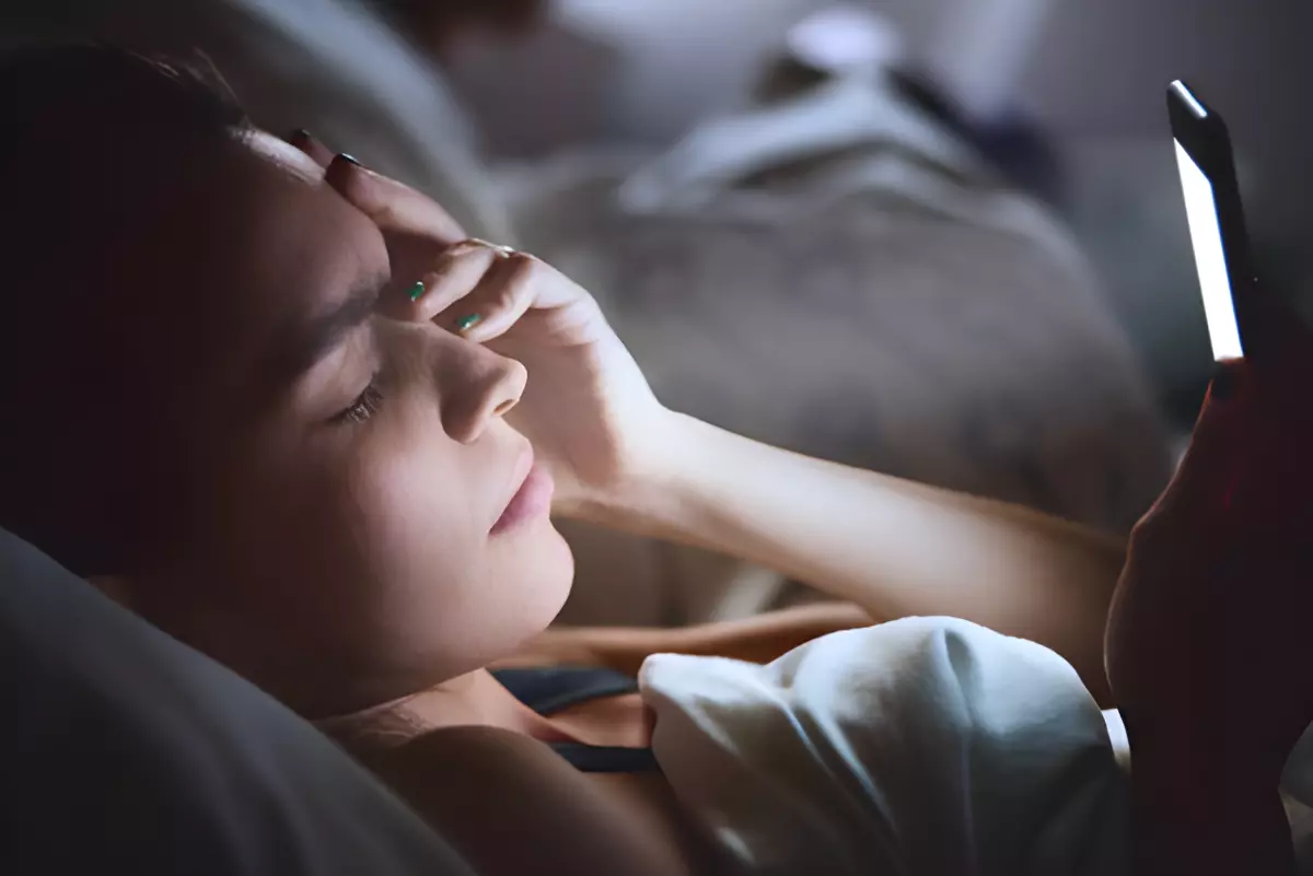 femme dans son lit se tient la tete avec une main avec l autre un telephone portable qui eclaire son visage