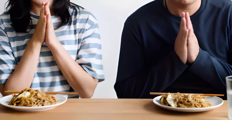 femme et homme devant leur assiettes avec des mains jointes