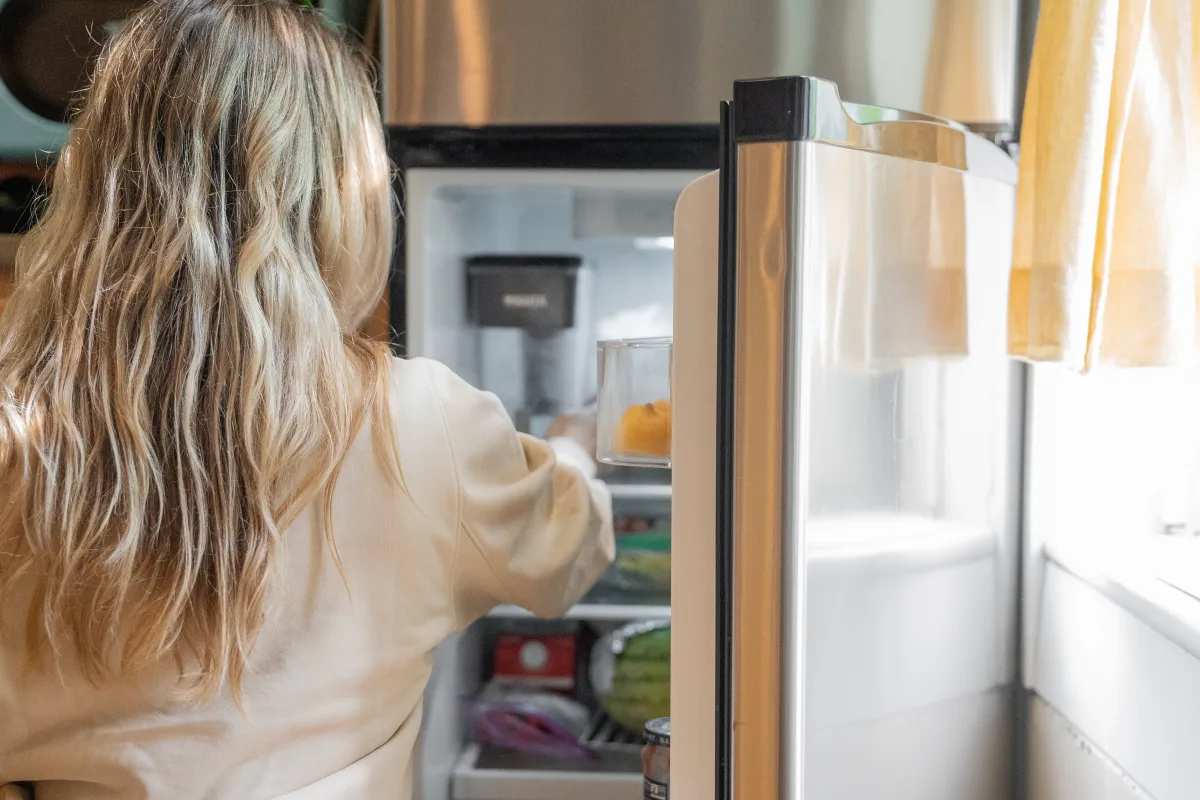 femme porte ouverte refrigerateur aliments lumiere cuisine serviette cheveux blonds