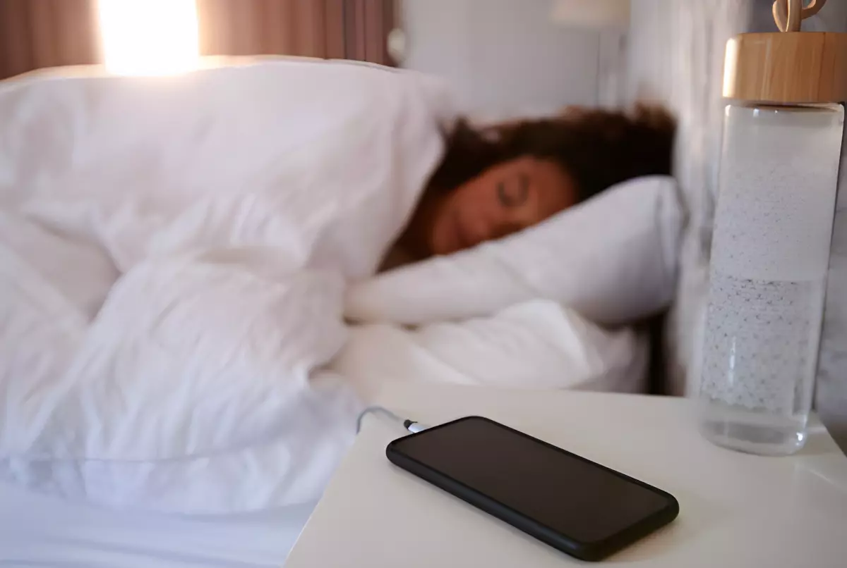 femme qui dort dans un lit aux draps blanc et telephone portable portable qui se charge pose sur la table de nuit
