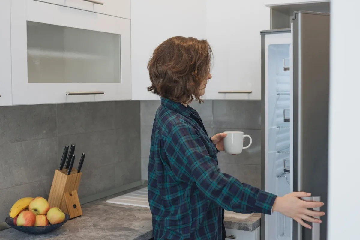 femme tasse cafe porte frigo ouverte plan travail aspect pierre gris anthracite