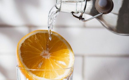 la moitie d un citron coince sur la partie haute d un verre avec un fil de eau qui passe dessus depuis une bouteille en verre