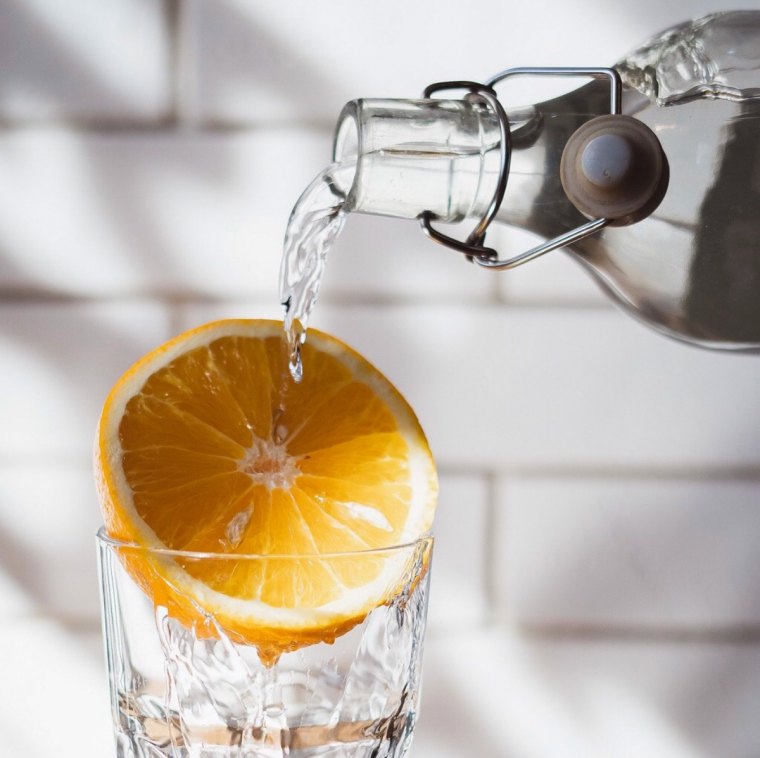 la moitie d un citron coince sur la partie haute d un verre avec un fil de eau qui passe dessus depuis une bouteille en verre