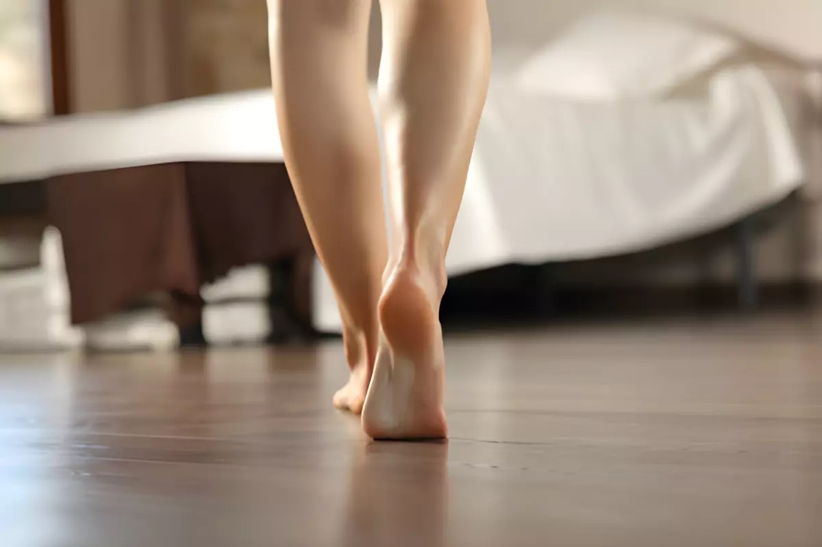 pieds nus de femme qui marche de dos vers un lit sur un parquet