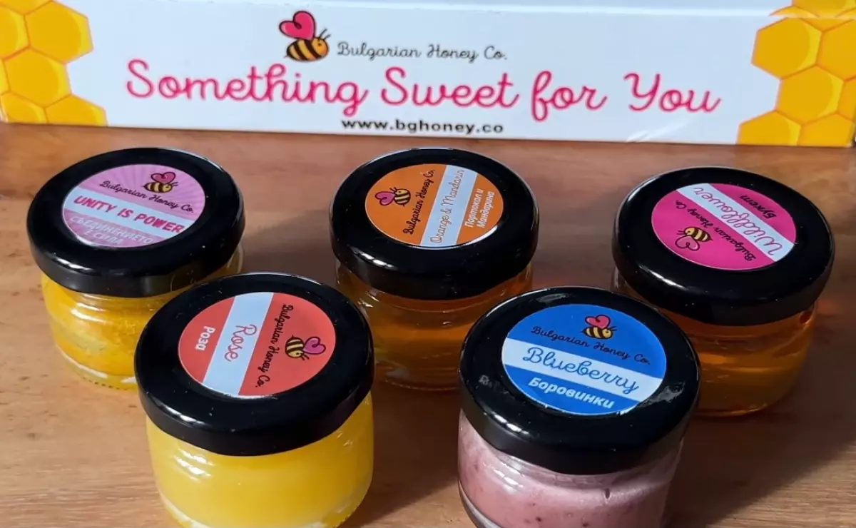 cinq petits bocaux de miel de differnetes couleurs devant leur boite en arriere plan
