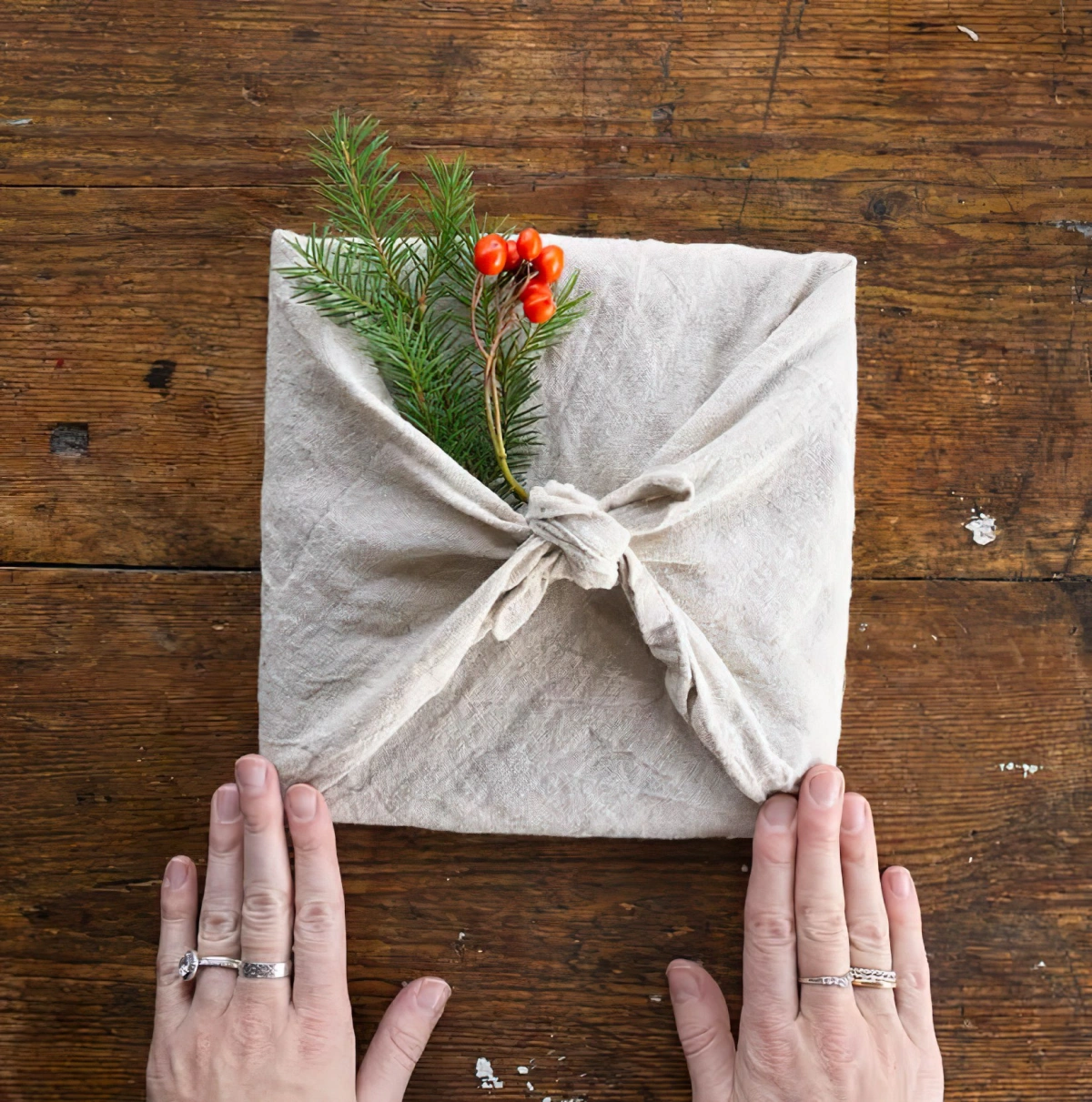 emballage furoshiki cadeau surface bois tissu beige mains branche pin