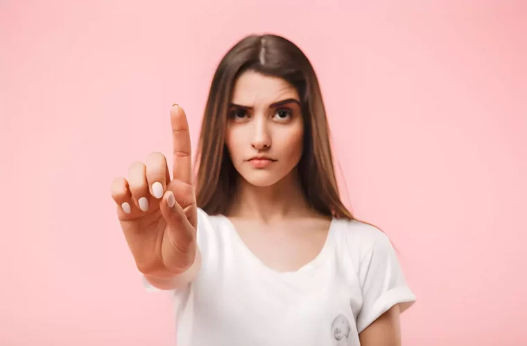 femme sur fond rose avec la main etendue devant elle avec l index redresse