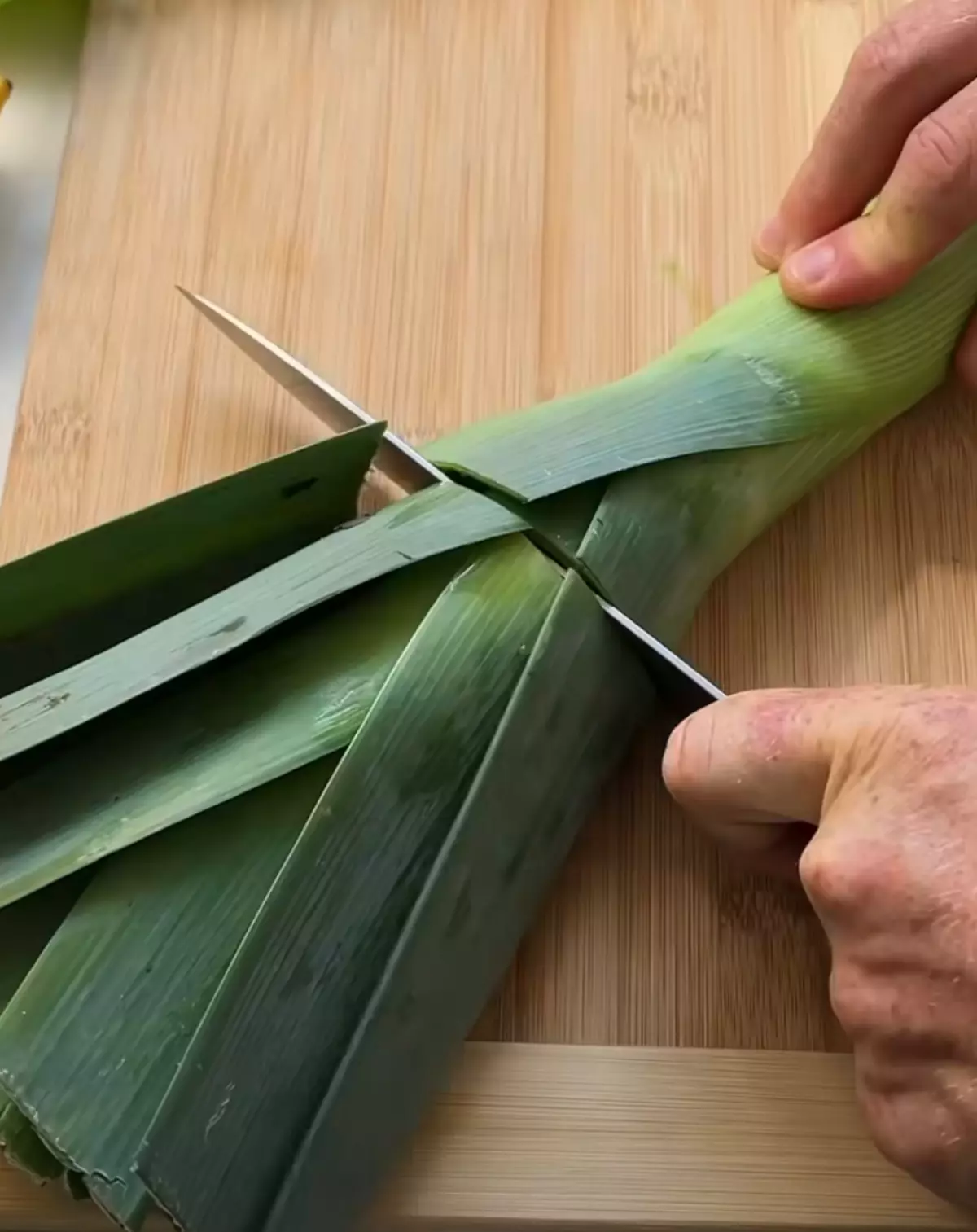 feuilles vertes du poireau avec un couteau enfonce sur une planche en bois