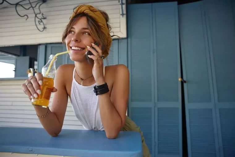 fille en ete souriante parle au telephone et tient avec une main une bouteille avec une paille
