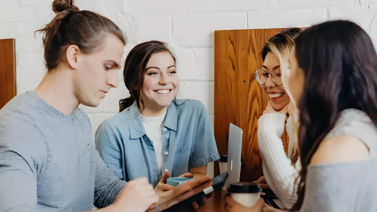 groupe de trois filles et un garcon assis a table dans un cafe parlent et rigolent