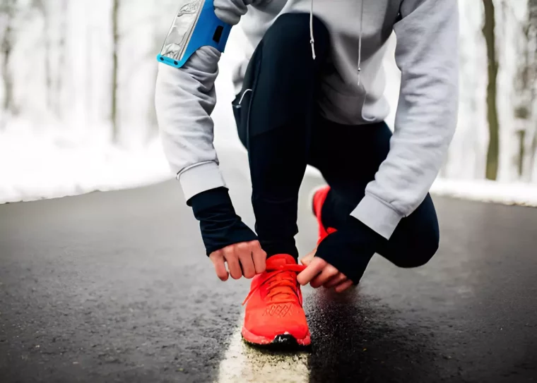 homme qui serre les lacets de ses chaussures de sport rouges sur une voie goudronnee